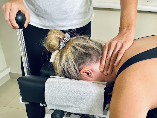 Fizjoterapeuta wykonuje bezbolesną dekompresję szyjnego odcinka kręgosłupa na specjalistycznym stole Coxa. Pacjent leży wygodnie na brzuchu, a terapeuta delikatnie rozciąga i mobilizuje kręgosłup szyjny, aby odciążyć uciśnięte nerwy i zredukować ból.
