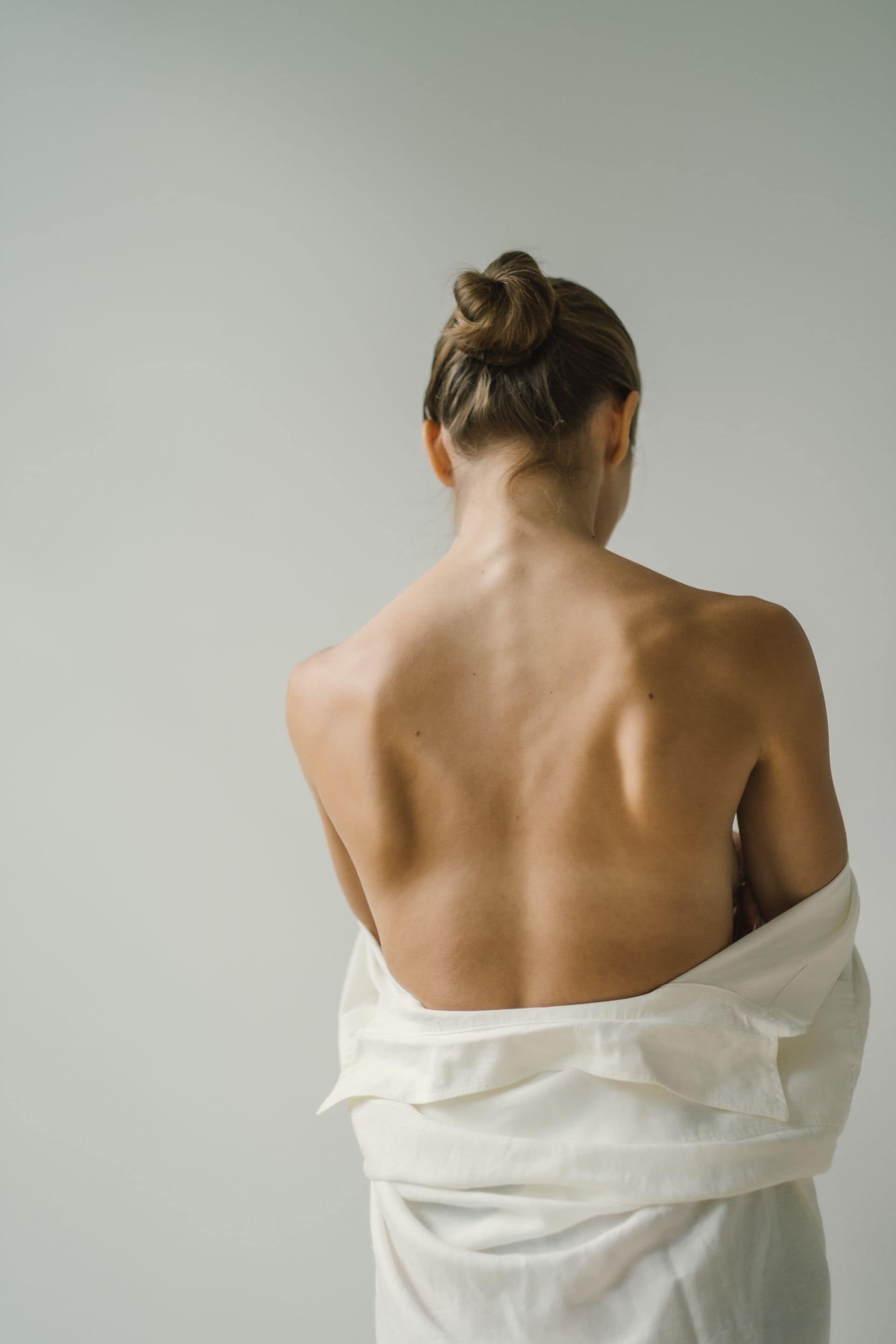 Fotografia przedstawia kobietę ustawioną tyłem do obiektywu, z odsłoniętymi plecami. Sygnalizuje ból i napięcie w odcinku lędźwiowym.